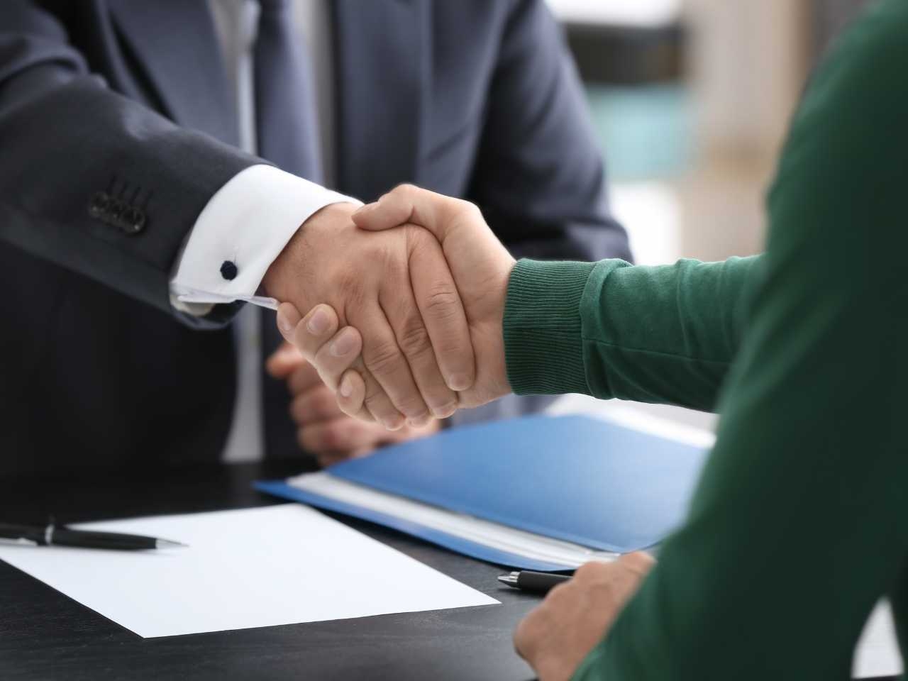 a client reaches across a desk to shake hands with a lawyer