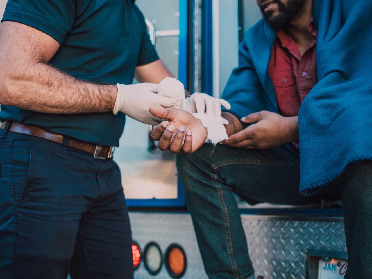 a man sits in the back of an ambulance getting his wrist injury wrapped up