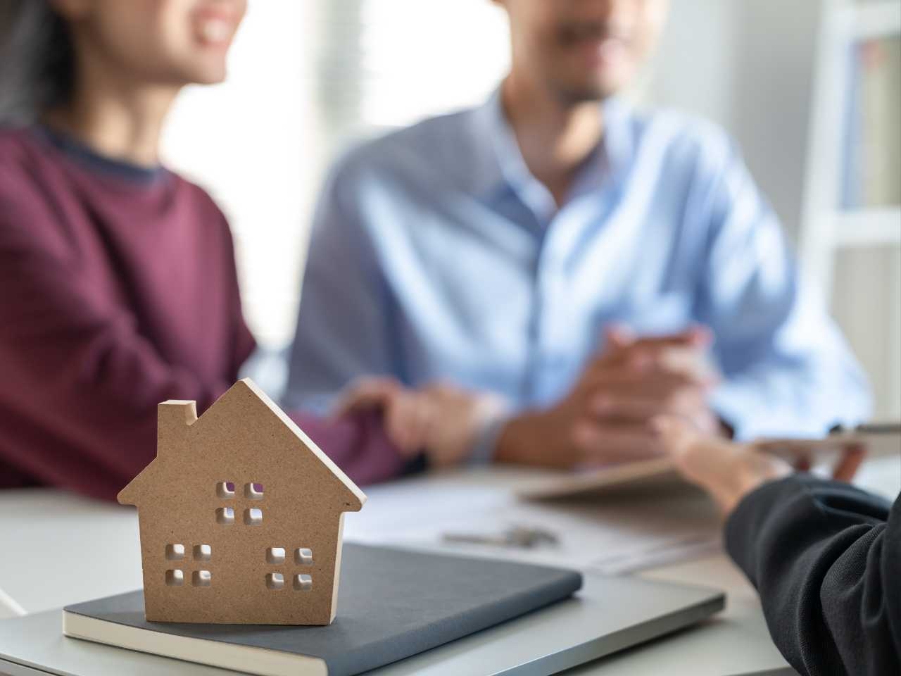 a couple speaks with their lawyer with a small house sitting on the desk